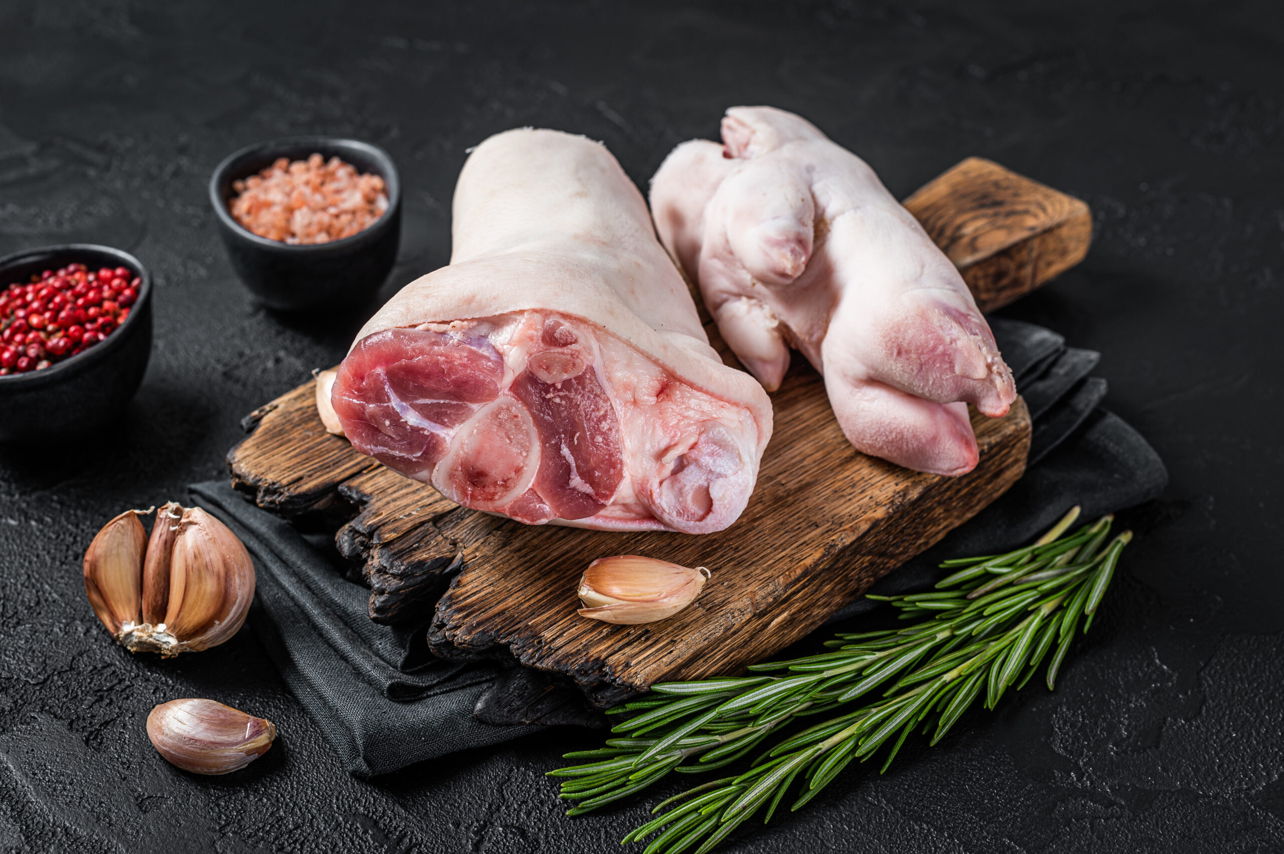 Raw pork knuckle or hoof, feet on a cutting board. Black background. Top view